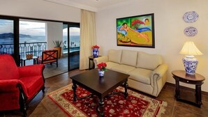 Una habitación con un sofá rojo, un sofá color beige, una mesa de centro, un cuadro y vistas al mar.