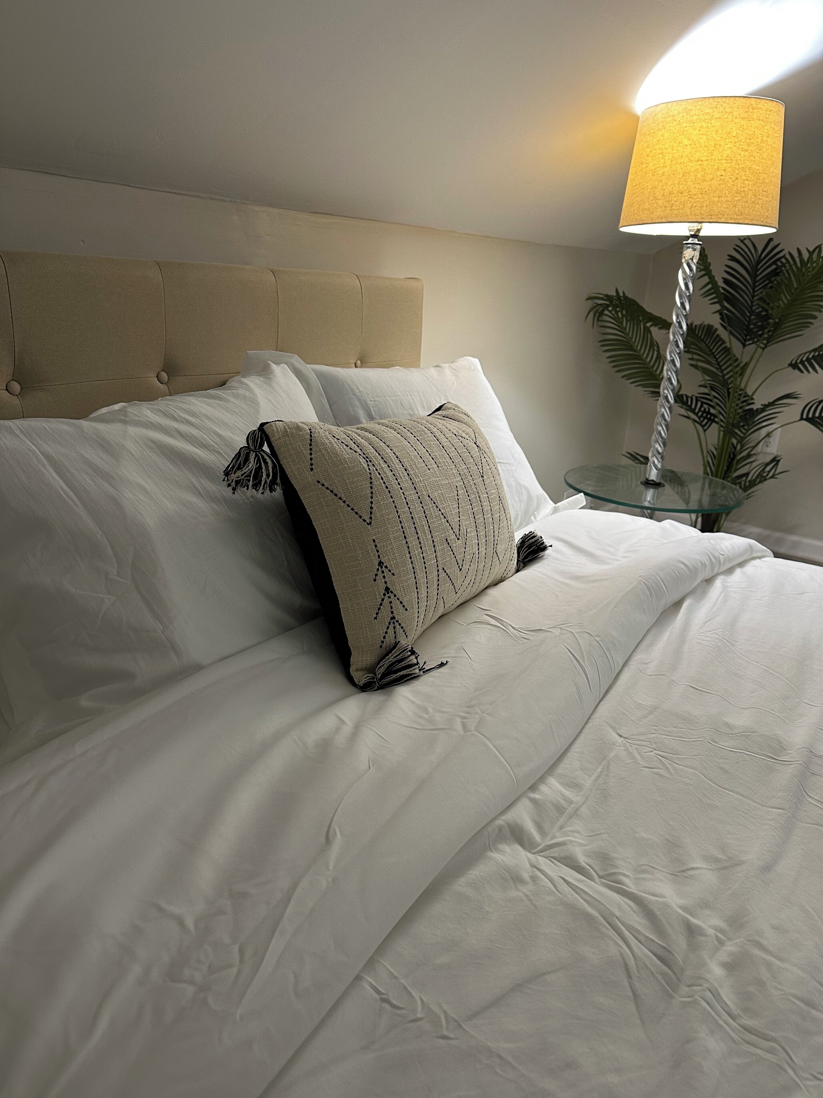 A neatly made bed with white linens and a decorative pillow.