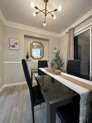 A dining area with a glass table, black chairs, a decorative mirror, and a ceiling light fixture. - Modern 3-bedroom house with WiFi and AC in North Rosedale Park (Detroit)
