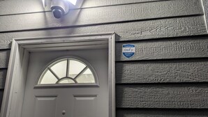 A white door with a semi-circular window and a security camera mounted above it.