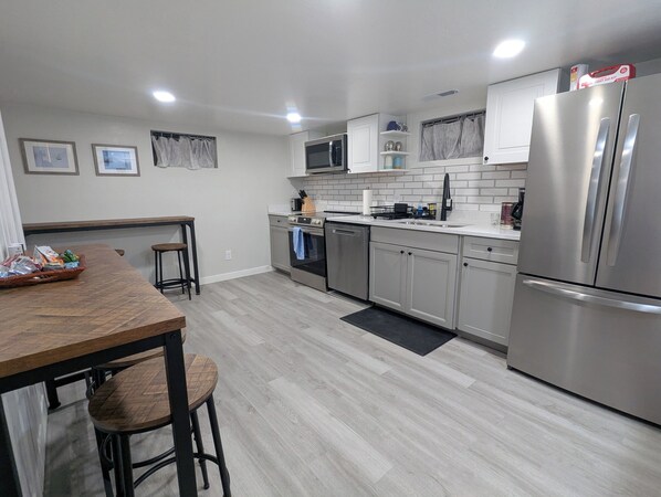 Una cocina moderna con electrodomésticos de acero inoxidable, una mesa de comedor de madera y un taburete de bar.