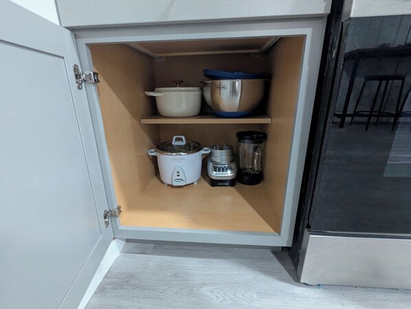 Un armario de cocina con un cocedor de arroz, una licuadora y una olla en los estantes.