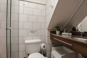 Une salle de bain moderne avec des carreaux blancs, des toilettes, un lavabo doté d’un plan de travail en marbre et un miroir.
