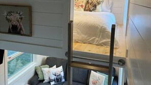 Ein Schlafzimmer im Loft-Stil mit einem Etagenbett, einem grauen Sofa mit Blumenkissen, einem weißen Nachttisch und einem gerahmten Bild an der Wand.