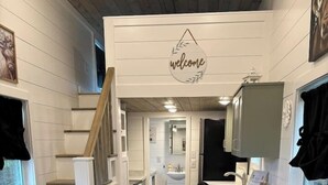 Eine kompakte Küche mit einer Holztreppe, einem Willkommensschild und Blick auf das angrenzende Badezimmer.