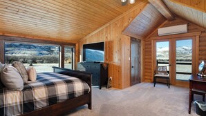 A log cabin bedroom with a bed, a TV, a desk, and a view of the mountains. - SPACIOUS & Stunning 6-bedroom Log Cabin Home Great for Large Gatherings! (Emigrant)