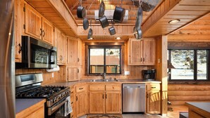 A wooden cabin kitchen with a stove, refrigerator, microwave, and hanging pots. - SPACIOUS & Stunning 6-bedroom Log Cabin Home Great for Large Gatherings! (Emigrant)