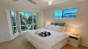 A bedroom with a bed, a ceiling fan, a nightstand, a lamp, and a window with a view of trees.