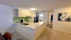 A modern kitchen with white cabinets, a central island, and a dining area with a red chair.