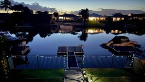 A waterfront property with a dock, a small boat, and a well-lit pathway leading to a gated entrance.