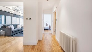 A modern, well-lit hallway with wooden flooring, a grey sofa with white cushions, and a radiator on the right. - 2Bedr/3Beds/2Bath Covent Garden 3min subway (London)