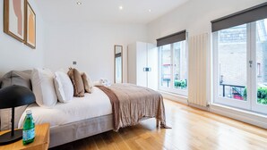 A modern bedroom with a large bed, a bedside table with a lamp, and a window with a view of a brick building. - 2Bedr/3Beds/2Bath Covent Garden 3min subway (London)