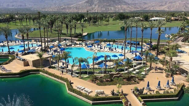 Ein Resort mit mehreren Schwimmbecken, Palmen und einem Golfplatz im Hintergrund.