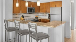 Eine moderne Küche mit Holzschränken, Edelstahlgeräten, einer Granitabdeckung und Barhocker.