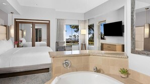 Ein Hotelzimmer mit einem großen Bett, einer Badewanne, einem Fernseher und Blick auf Palmen.