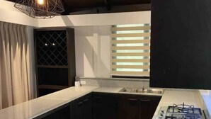 Uma cozinha moderna com armários escuros, bancada branca, fogão a gás e luminária pendente.