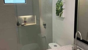 Uma casa de banho moderna com cabine de duche em vidro, sanita e lavatório com bancada de granito.