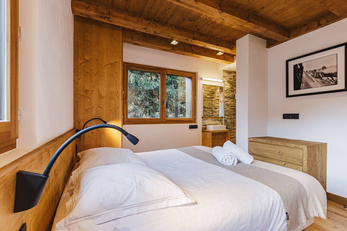Une chambre à coucher avec une tête de lit en bois, une grande fenêtre, une commode en bois et un tableau encadré accroché au mur.