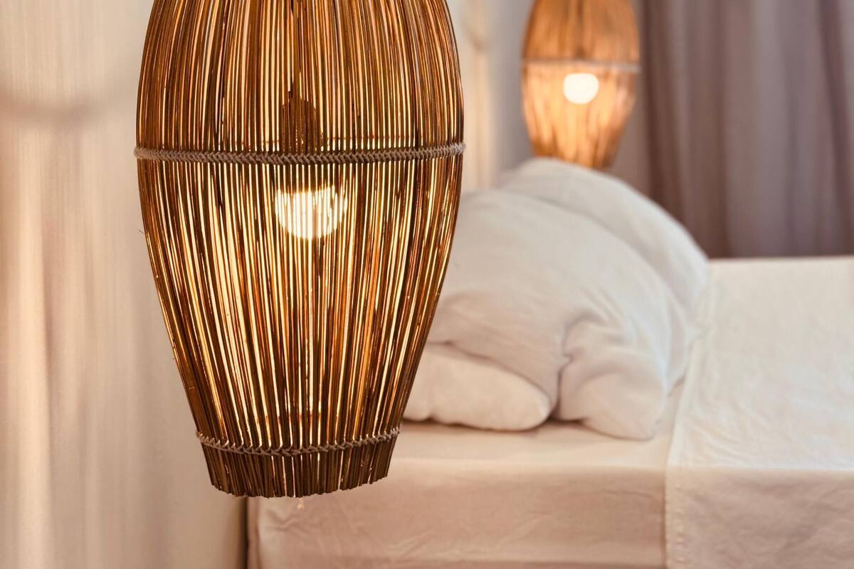 A room with a bed, a hanging rattan lamp, and a wall-mounted lamp.