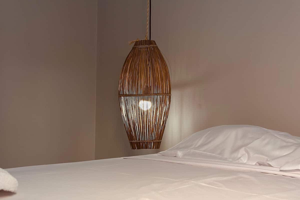 A bed with white linens and a hanging woven light fixture.