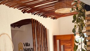 Ein Villa-Eingang mit einer Holztür, einem gewobenen Bambus-Bildschirm und dem Logo von Villa Manzu.