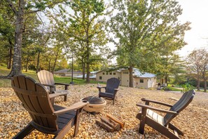 A patio with Adirondack chairs, a fire pit, and a house in the background.