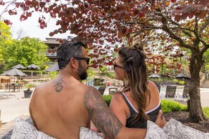 Una pareja sentada en un banco con una piscina y sombrillas al fondo.
