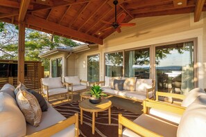 Eine Terrasse im Freien mit Holzmöbeln, einem Deckenventilator und großen Fenstern mit Blick ins Grüne.