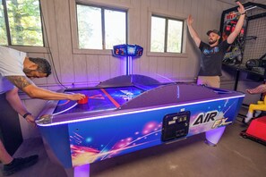 A pool table with a neon sign, a basketball hoop, and a scoreboard in a room with wooden walls and windows.