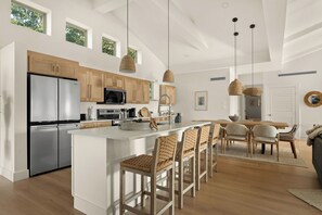 A modern kitchen with a central island, wooden cabinets, stainless steel appliances, and a dining area with wicker chairs.