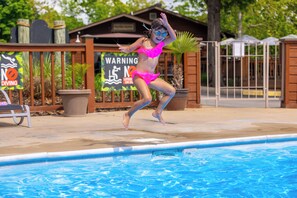 Un niño salta a una piscina, con un cartel de advertencia al fondo.