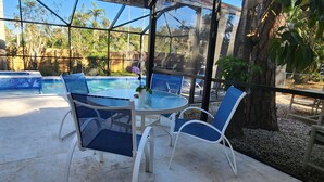 Ein überdachter Patio-Bereich mit Pool, Sitzgelegenheiten im Freien und Blick auf die umliegende Bepflanzung.