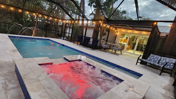 Ein Schwimmbecken mit Whirlpool, umgeben von Liegestühlen und Lichterketten.