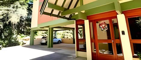 A building with a green and beige facade, a covered entrance, and a parked car in the background.