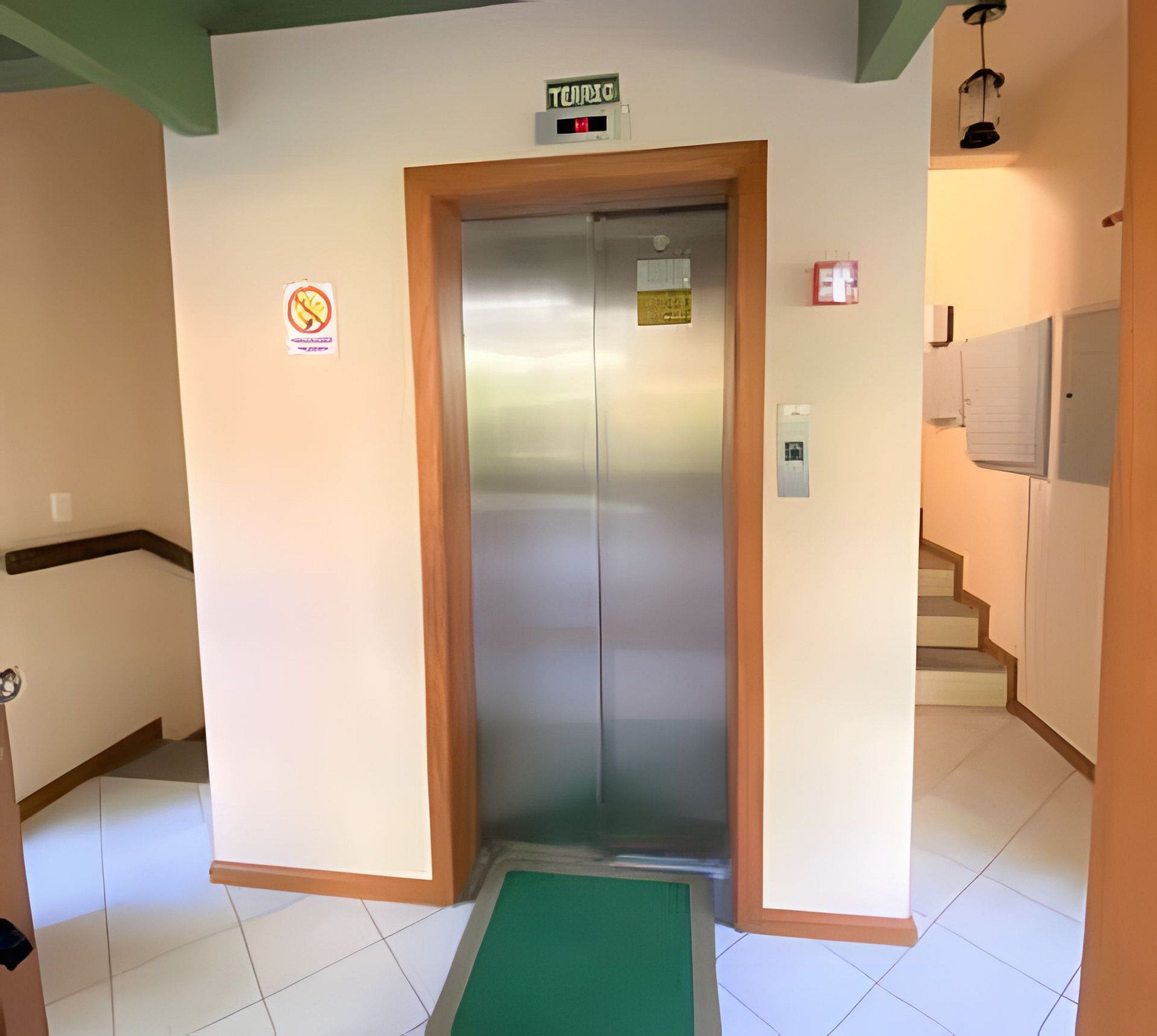 Un ascensor con un cartel encima y un letrero de prohibido fumar en la pared, además de un pequeño cartel en la puerta del ascensor.