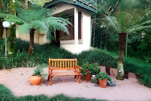 Un banc en bois dans un jardin, avec des plantes en pot et un petit bâtiment doté d’un toit végétalisé.