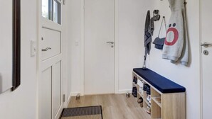 Um corredor com uma porta branca, um banco com sapatos e toalhas penduradas na parede.