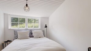Quarto com uma cama grande, uma janela com vista para área verde, uma luminária pendente e um abajur.