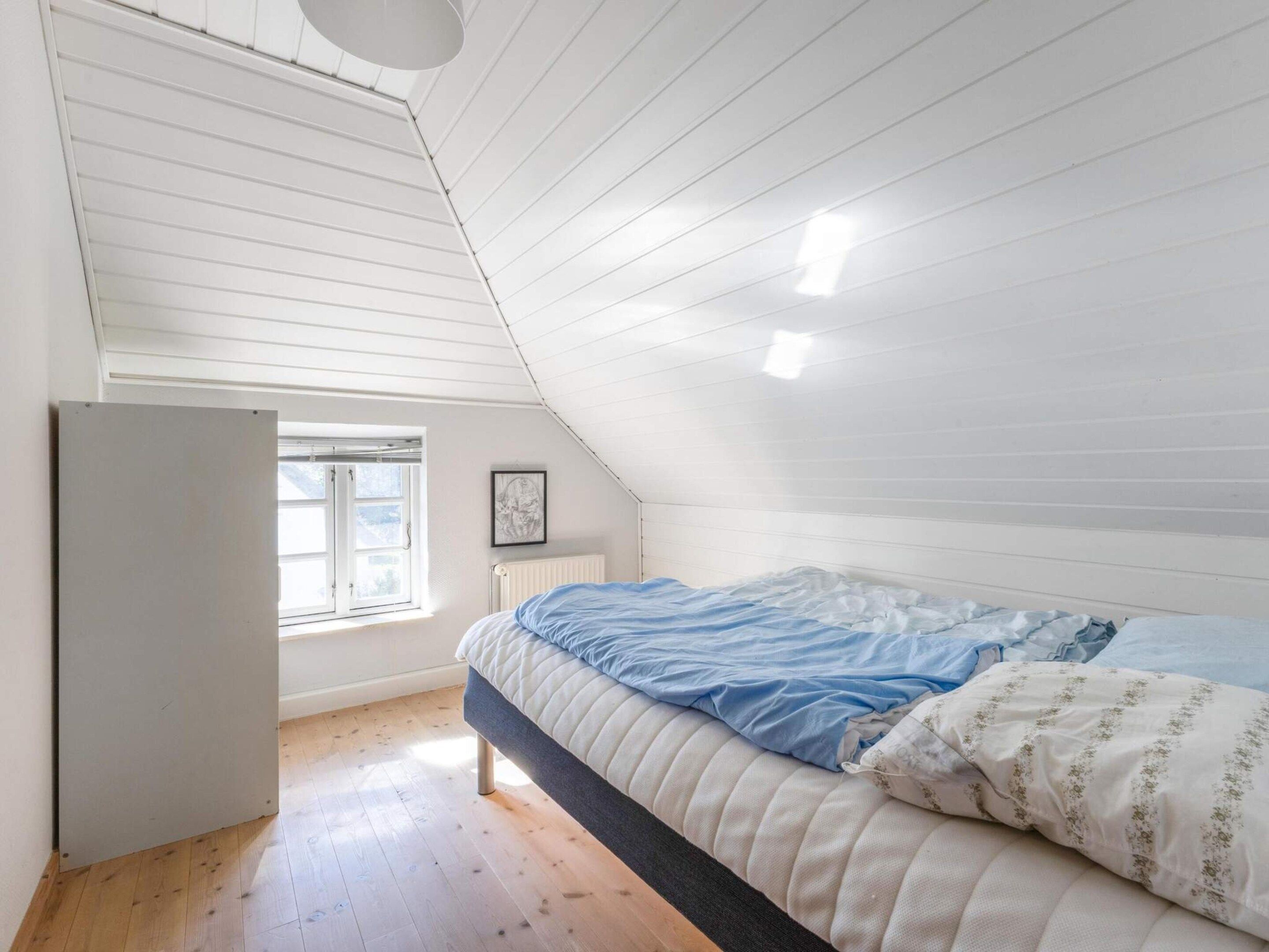 A bedroom with a sloped ceiling, a bed with a blue and white duvet, a radiator, and a window with a view.