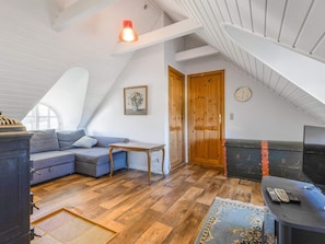 A loft-style room with a sloped ceiling, wooden flooring, a sofa, a small table, and a door. - 5 Star Holiday Home in Blokhus (Blokhus)
