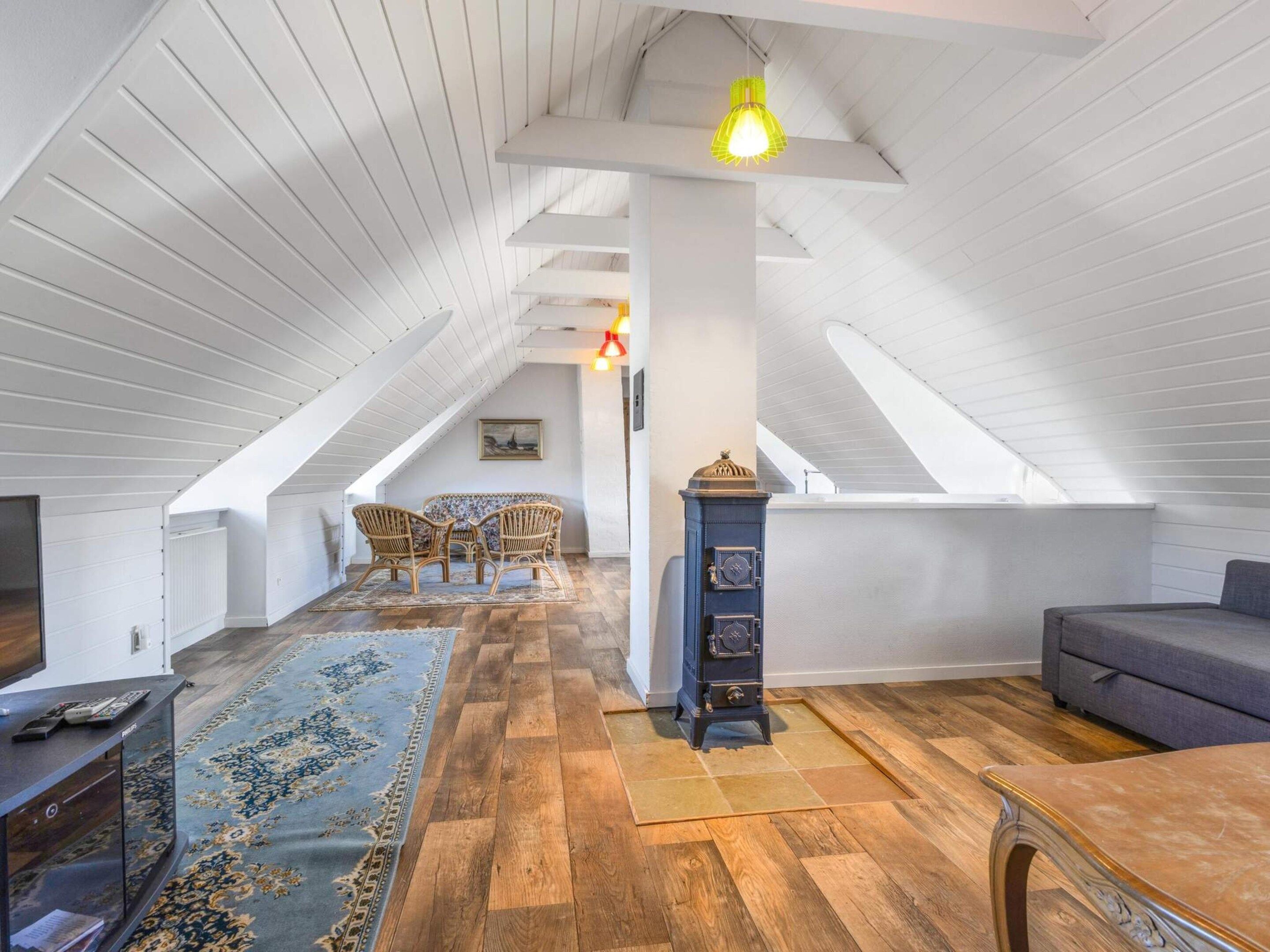 A spacious attic room with a sloped ceiling, a wooden floor, a sofa, a dining table, and a decorative clock.