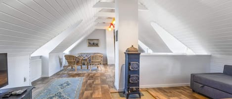 A spacious attic room with a sloped ceiling, a wooden floor, a sofa, a dining table, and a decorative clock.