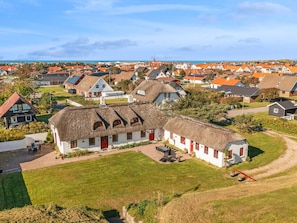 A traditional thatched-roof house with a red door, surrounded by a well-maintained lawn and a paved driveway.