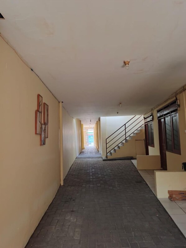 Un largo y estrecho pasillo con suelo de ladrillo y una escalera a la derecha.