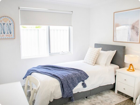 A bedroom with a bed, a nightstand, a chair, a window with blinds, and a wall decoration.