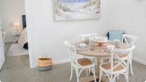 A dining area with a round wooden table, white chairs, and a beach-themed painting on the wall. - Welcome to Bay Belle - Binalup (MIDDLETON BEACH)