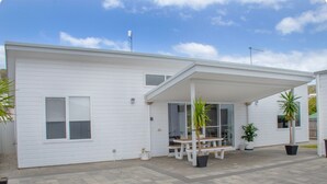 A modern white house with a covered patio, a wooden bench, and potted plants. - Welcome to Bay Belle - Binalup (MIDDLETON BEACH)