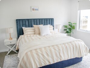 A bedroom with a bed, bedside tables, a nightstand, a window, and a plant.
