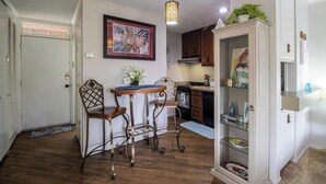A compact kitchen with a dining area, featuring a table with chairs, a hanging light fixture, and a cabinet with glass doors.