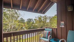 A covered outdoor deck with two chairs and a table, overlooking a garden and trees.